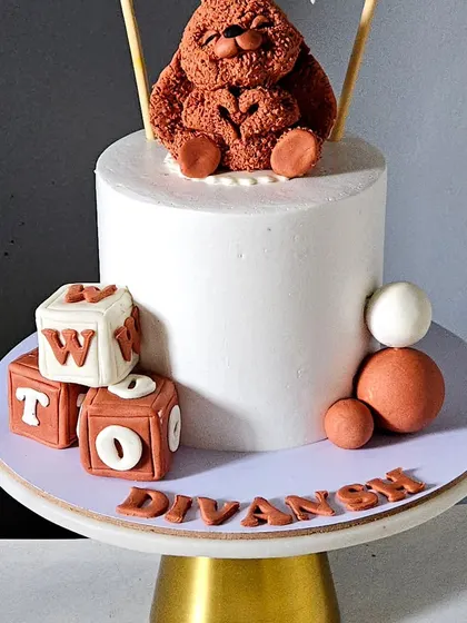 A minimalist and cute bunny-themed cake for a second birthday. The cake is topped with a handcrafted bunny with a unique textured "fur" effect and edible letter blocks.