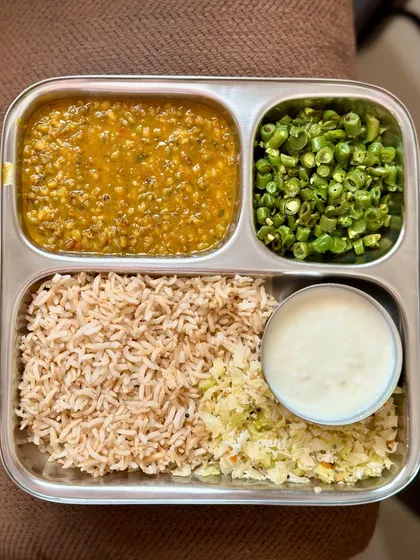 A wholesome plate of brown rice, whole green gram dal, sautéed beans, and cabbage, with a side of curd.