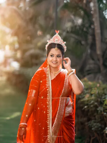 A radiant portrait of the Bengali bride in her striking red saree, glowing in the soft sunlight.