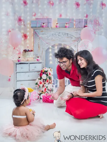 A sweet family moment during a first birthday photoshoot. The parents are looking lovingly at their baby girl, who is the center of attention in this beautiful celebration.