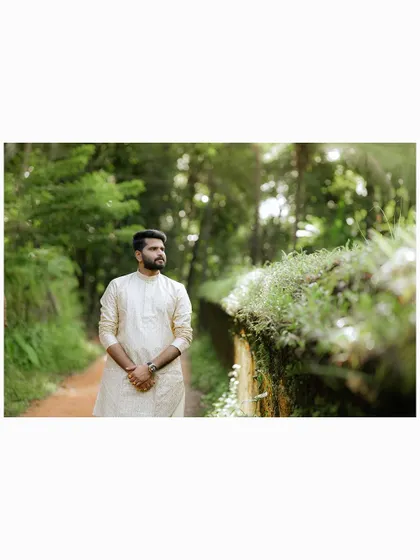 A portrait of the groom walking down a path, surrounded by lush greenery.