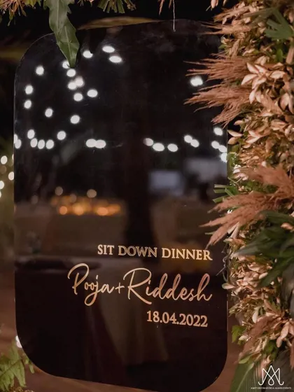 A chic and simple welcome sign for a sit-down dinner, with elegant calligraphy on a dark, reflective surface, framed by pampas grass.