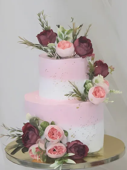 This two-tiered cake is a vision of floral elegance, with a pink and white ombre effect. It's beautifully decorated with a mix of deep red and soft pink sugar flowers, creating a rich and romantic look for any celebration.