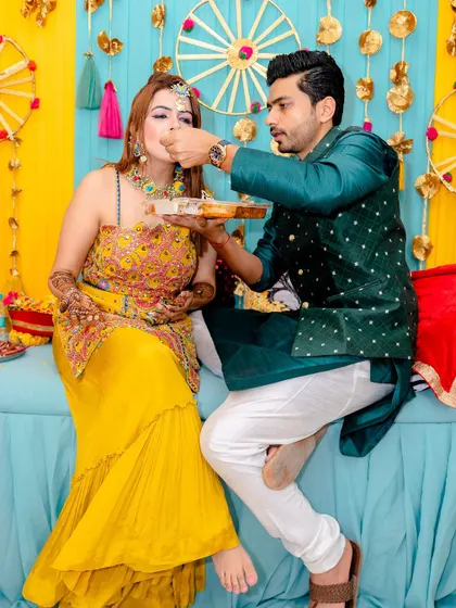 A sweet moment where the groom feeds the bride during the mehendi ceremony.