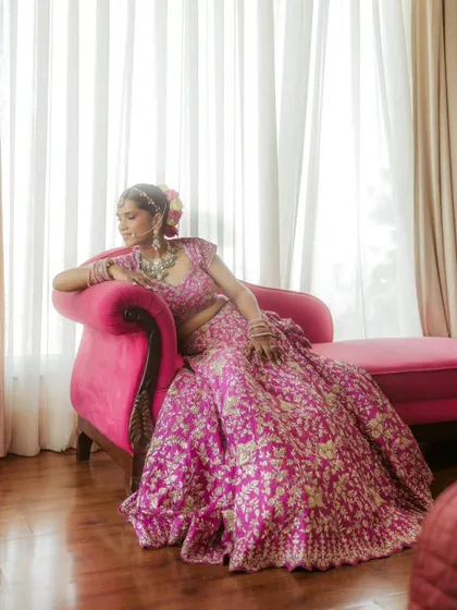 A portrait of modern royalty. Bride Jhalak relaxes on a vibrant pink chaise lounge, her magnificent pink lehenga creating a stunning monochromatic look.