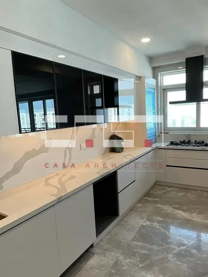 A sleek, all-white modern kitchen under construction, showing the clean lines of the handleless cabinets, marble-patterned countertops, and integrated sink.