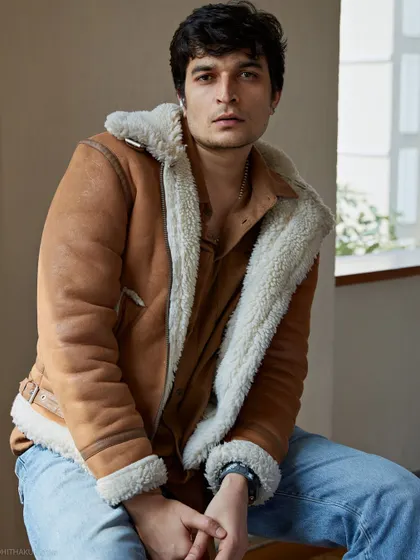 A warm and inviting male portrait. The shearling jacket adds texture and a sense of comfort, while the natural light from the window creates a soft, approachable look.