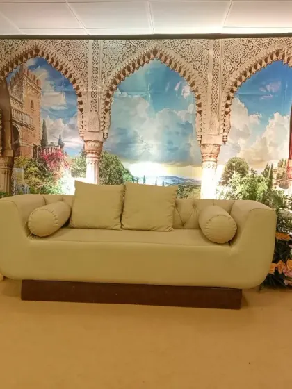 A themed stage backdrop featuring a print of scenic Moroccan arches. The setup is completed with a comfortable sofa and floral arrangements, transporting guests to another place.