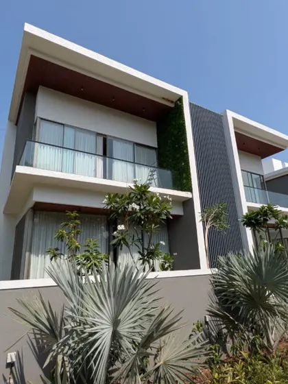 A site photo of a beautiful bungalow project in Lonavala. The design features clean, modern massing with contrasting materials, a green wall, and large windows that connect the interior with the surrounding nature.