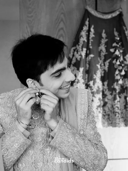 A playful black and white shot of the groom helping his bride with her earring, a sweet, candid moment during the getting-ready process.