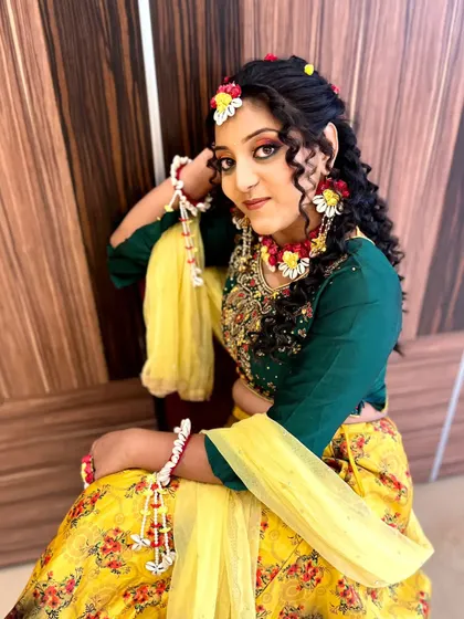 A full portrait of a model in a beautiful Haldi look, with curly hair and floral jewelry complementing the colorful eye makeup.