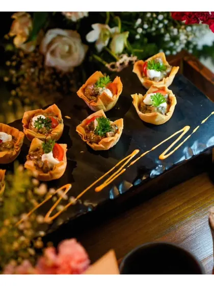 Bite-sized tartlets with a savoury filling, artfully arranged on a slate platter with a drizzle of sauce.