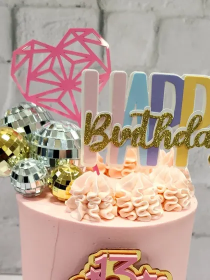 A close-up of the colorful "Happy Birthday" topper and mini disco balls that give this teenage birthday cake its party vibe.