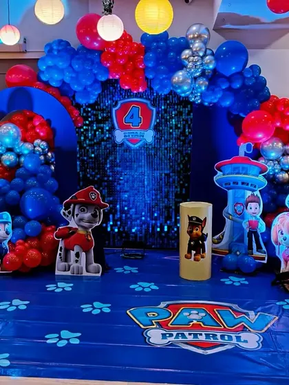 A 'Paw Patrol' themed birthday party, ready for action. The setup features a full cast of character cutouts, a themed floor mat, and a red and blue balloon arch against a shimmering backdrop.