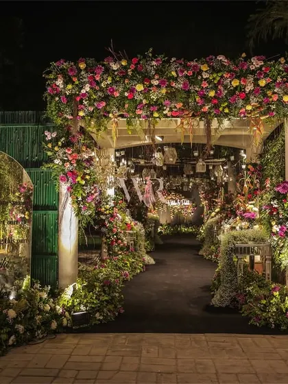 The entrance from the outside, featuring a grand floral arch and a mirrored sign to welcome guests. The design seamlessly blends the built structure with the surrounding nature.