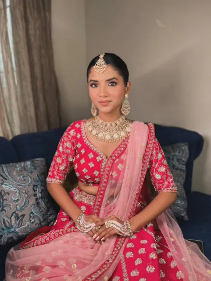 A full view of the elegant bridal look. The makeup is perfectly balanced with her stunning jewelry and pink and red lehenga, creating a cohesive and regal appearance.