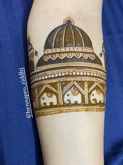 A close-up of the trending dome-style beginning. This architectural motif, complete with tiny elephants, is a grand and popular way to start a full bridal arm design.
