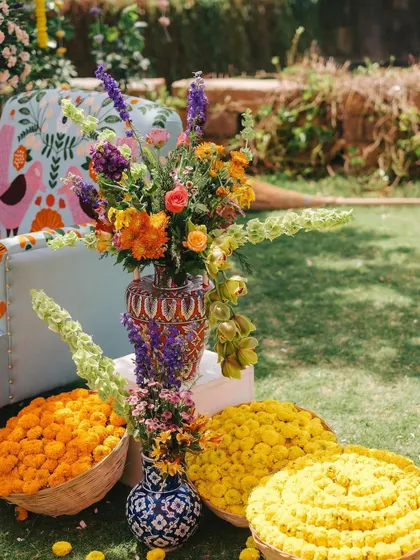 A vibrant floral arrangement in a hand-painted vase, set beside baskets of fresh marigolds. This setup for a Mehandi event is a beautiful blend of traditional elements and modern floral artistry.