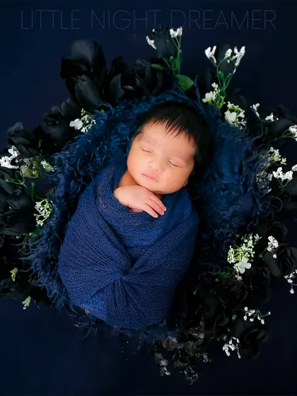 A newborn dreams among dark blue and white flowers. This artistic composition creates a beautiful contrast and a magical, night-sky feeling for an infant portrait.