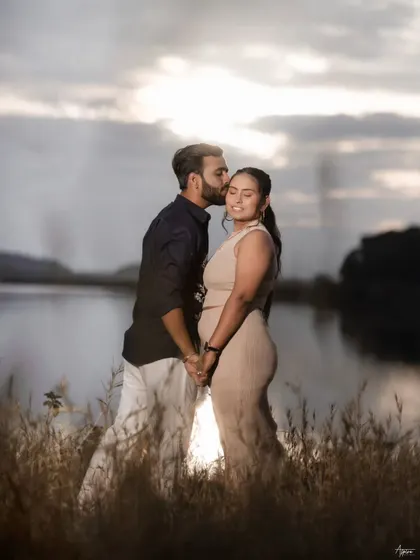 A romantic silhouette-style shot of Prem and Jinal against the setting sun. The warm light and the tender kiss on the forehead create a timeless and emotional image by the lake.