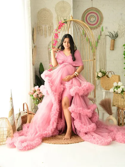 This solo portrait showcases the incredible detail and volume of our pink ruffled maternity gown. The mom-to-be is posed in our popular golden birdcage chair within the boho set.