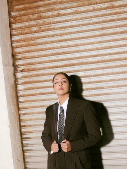 A full-body shot against a rustic shutter, where the strong silhouette of the suit creates a striking contrast.