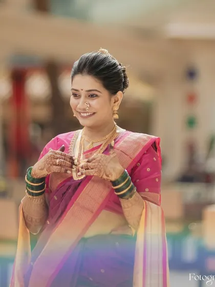 A beautiful portrait of a Marathi bride in her traditional pink and purple saree, smiling brightly.