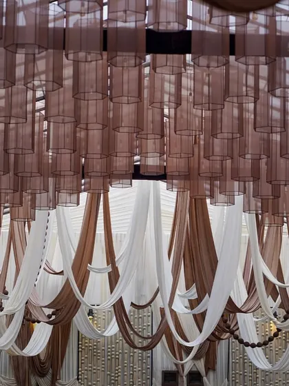 A wide view of the ceiling, showing how the combination of sheer brown lamp shades and draped fabrics in beige and brown creates a warm, intimate, and stylish canopy over the space.