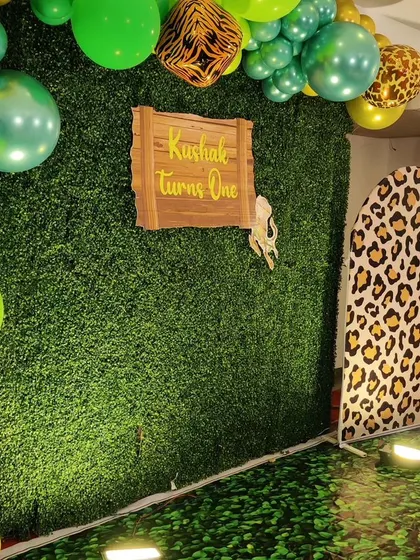 A jungle-themed photo booth corner with a lush green wall. This setup features a wooden sign, a leopard-print archway, and a leafy floor for the perfect photo opportunity.