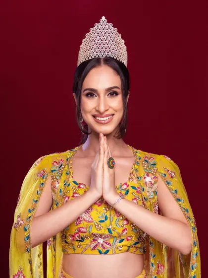 A portrait capturing the humility and grace of a winner. The 'namaste' pose and the crown create a powerful and inspiring image.