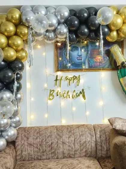 A simple yet elegant birthday setup for an adult. The black, gold, and silver balloon arch is paired with a champagne bottle foil balloon and fairy lights.
