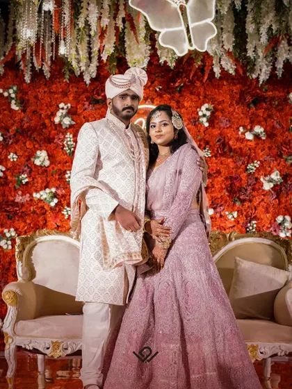 A formal stage portrait of a couple against a red floral backdrop.
