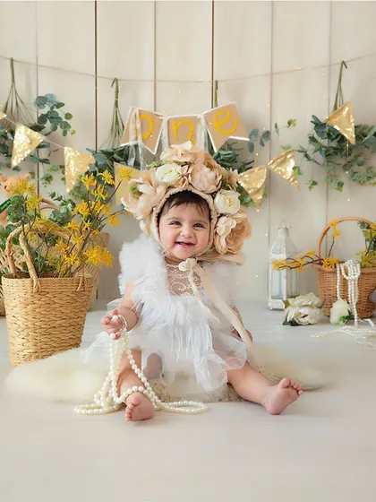This beautiful baby portrait captures a sweet, happy expression. The oversized floral bonnet and soft textures create a whimsical and artistic feel.