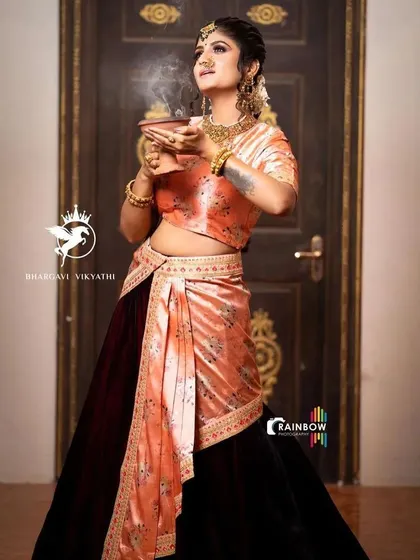 This unique Indo-Western set pairs a rich maroon velvet skirt with a peach floral printed top. The attached drape adds a touch of saree-like elegance to the modern silhouette.