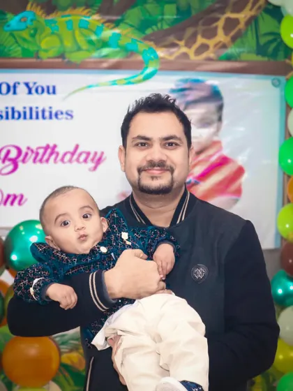 A father holds his baby, who is looking curiously at the camera during a birthday party. We are experienced in photographing babies and young children.