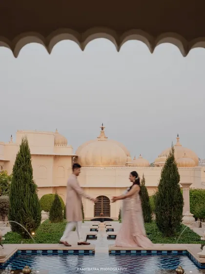 The couple reaches for each other across a water body in the palace courtyard, a romantic and symmetrical composition.