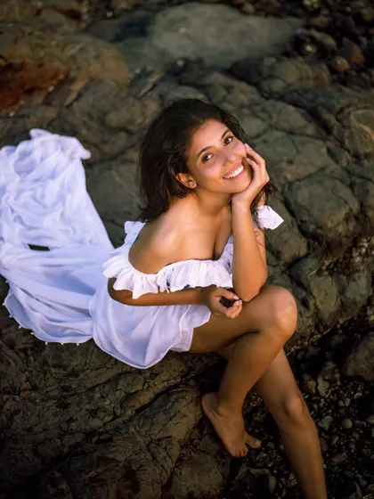 A happy, seated pose on the rocks, showcasing a relaxed and joyful side in this beautiful beach setting.
