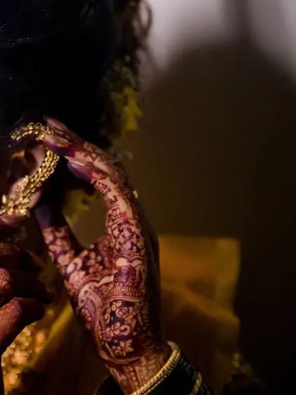 A close-up of the bride's hand as she adjusts her earring, showcasing her detailed henna and jewelry.