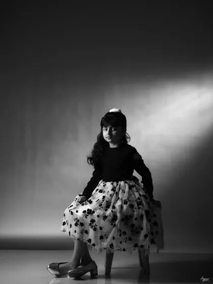 Seated and looking directly at the camera, this black and white portrait is simple yet captivating. The soft spotlighting creates a classic, elegant feel for this child's photoshoot.