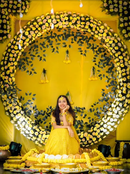 A stunning portrait of the bride seated amidst a grand circular backdrop of yellow marigolds for her Haldi ceremony.