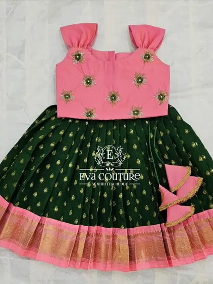 A sleeveless pattu pavadai in green and pink. The simple top has delicate butti work, and the green skirt has a classic gold and pink border.