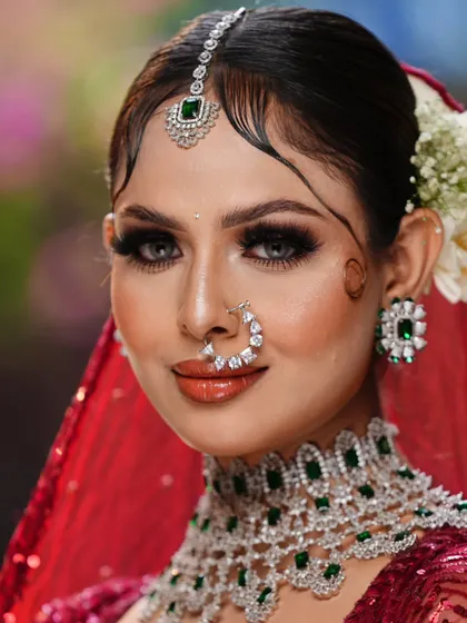 A captivating portrait of a bride in red. The focus is on her striking eyes, enhanced with full lashes and a flawless base. The emerald jewelry adds a beautiful contrast, making this a truly regal look.