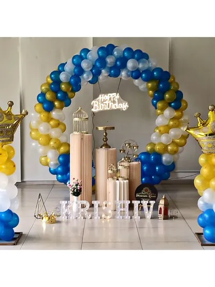 A prince-themed birthday setup with blue, yellow, and white balloons, and large crown props on balloon columns.