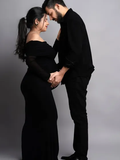 An elegant and classic maternity pose. The off-the-shoulder black dress is a timeless choice, and the couple's connection is the beautiful focus of the image.