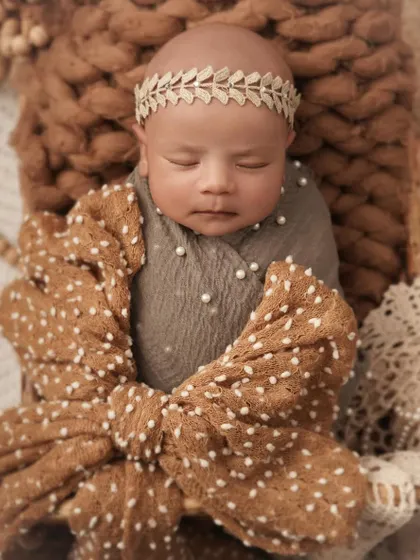 A sweet, sleeping portrait of a one-month-old baby, wrapped snugly with a large bow. The earthy tones and soft textures create a warm and comforting atmosphere.
