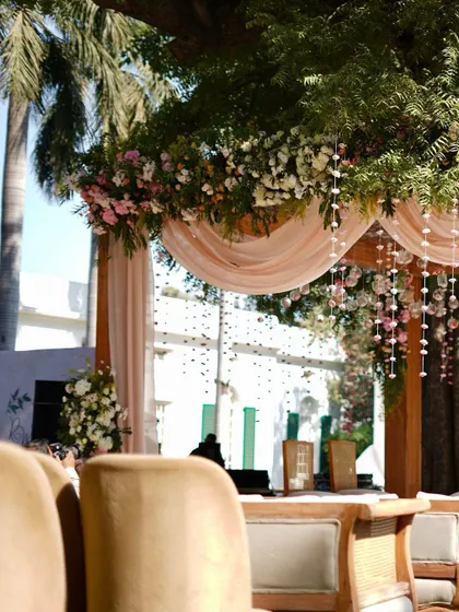 Another angle of the sun-kissed mandap, highlighting the soft, flowing drapes and the lush floral arrangements that blend seamlessly with the surrounding greenery.