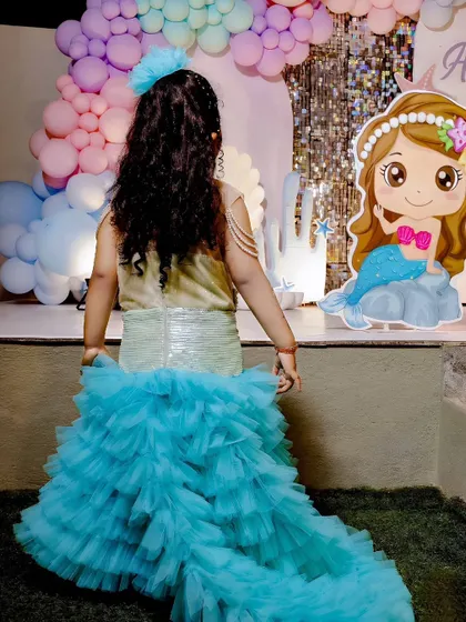 The birthday girl dressed in a stunning mermaid costume with a long, ruffled tail, perfectly matching her party's theme.