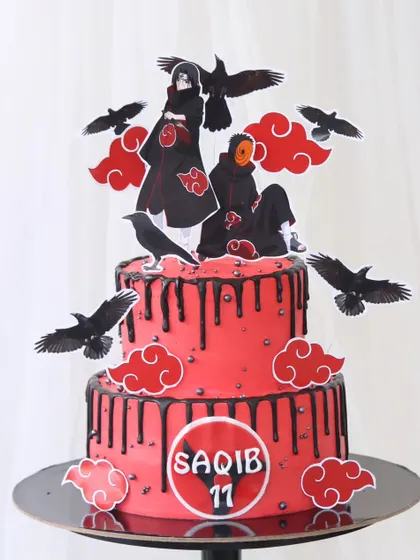 A dramatic two-tiered anime cake for a Naruto fan. The striking red cake features a black chocolate drip and is decorated with characters and symbols from the Akatsuki clan.