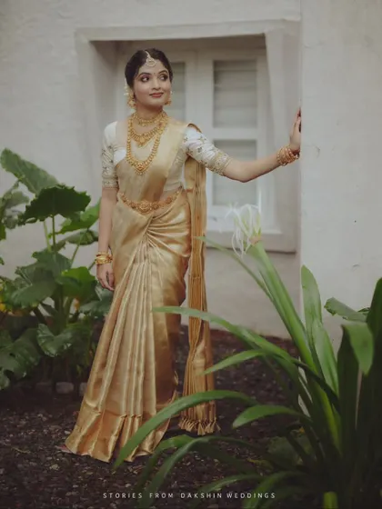 A full-length shot of a bride in her traditional Kerala wedding saree, standing in a garden.