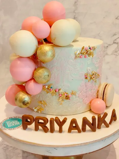 An elegant chocolate chip cake decorated with pink, white, and gold chocolate spheres and macarons. The delicate stenciling on the side adds a touch of sophistication.
